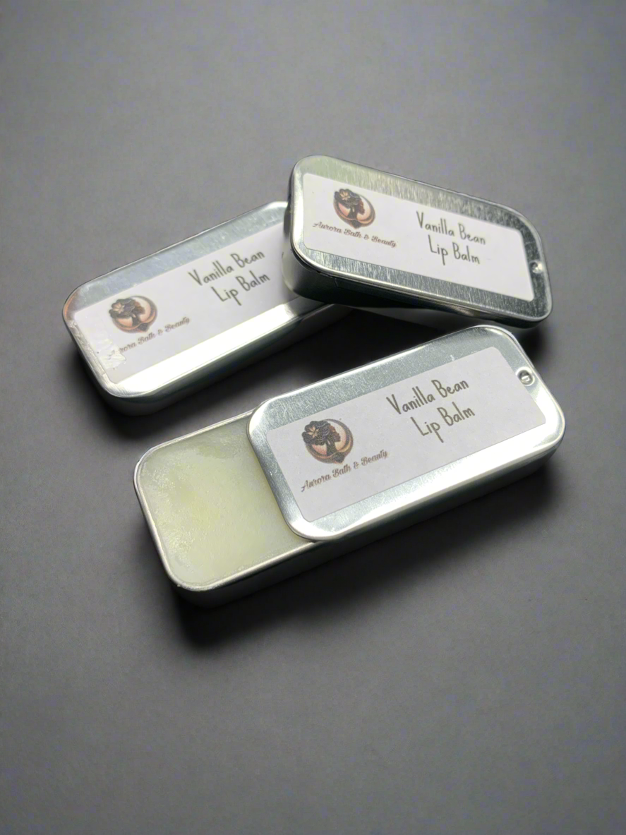 Three small metal lip balm tins with vanilla bean written on the labels, placed side by side on a dark background.