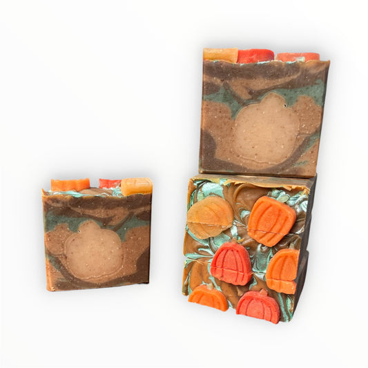 Five bars of soap with green, orange, and brown swirls, featuring orange pumpkin embeds stacked on a white background.