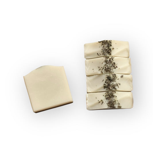 Stack of pale green soap bars with visible herbs on a white background