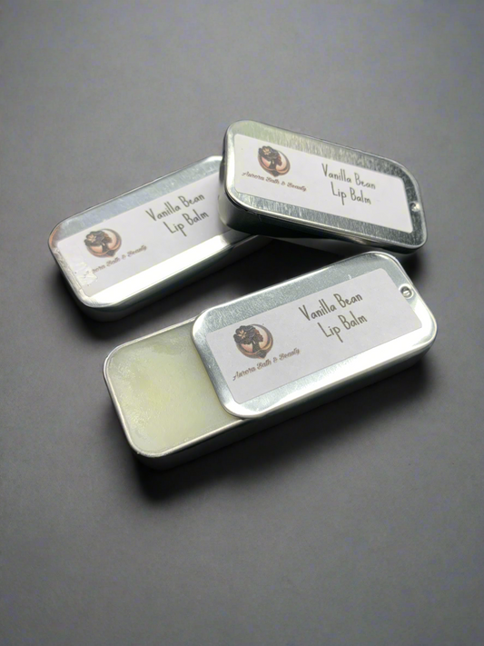 Three small metal lip balm tins with vanilla bean written on the labels, placed side by side on a dark background.