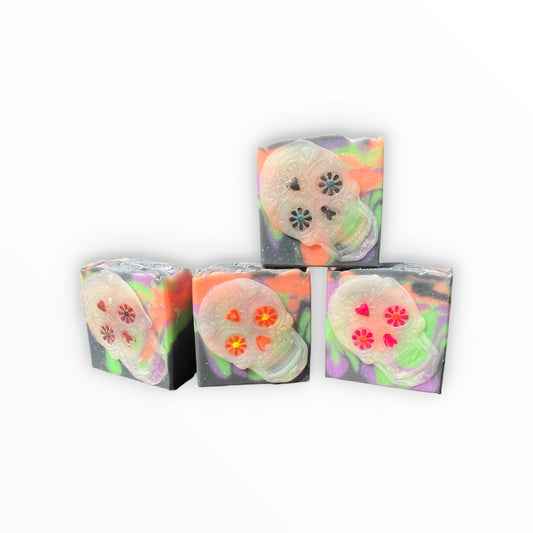 Four bars of soap, white black, orange, green and purple swirl designs stacked on a plain white background. The soaps feature a translucent sugar skull design with colorful neon accents in orange, pink, red, and black.